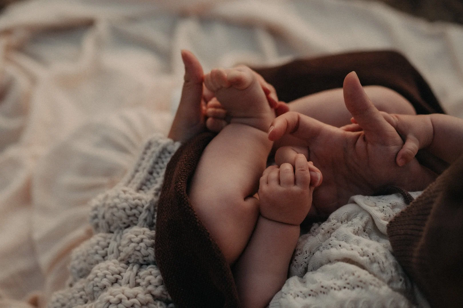 Ein Baby sitzt auf Mamas Schoß und umschließt Mamas Hände.