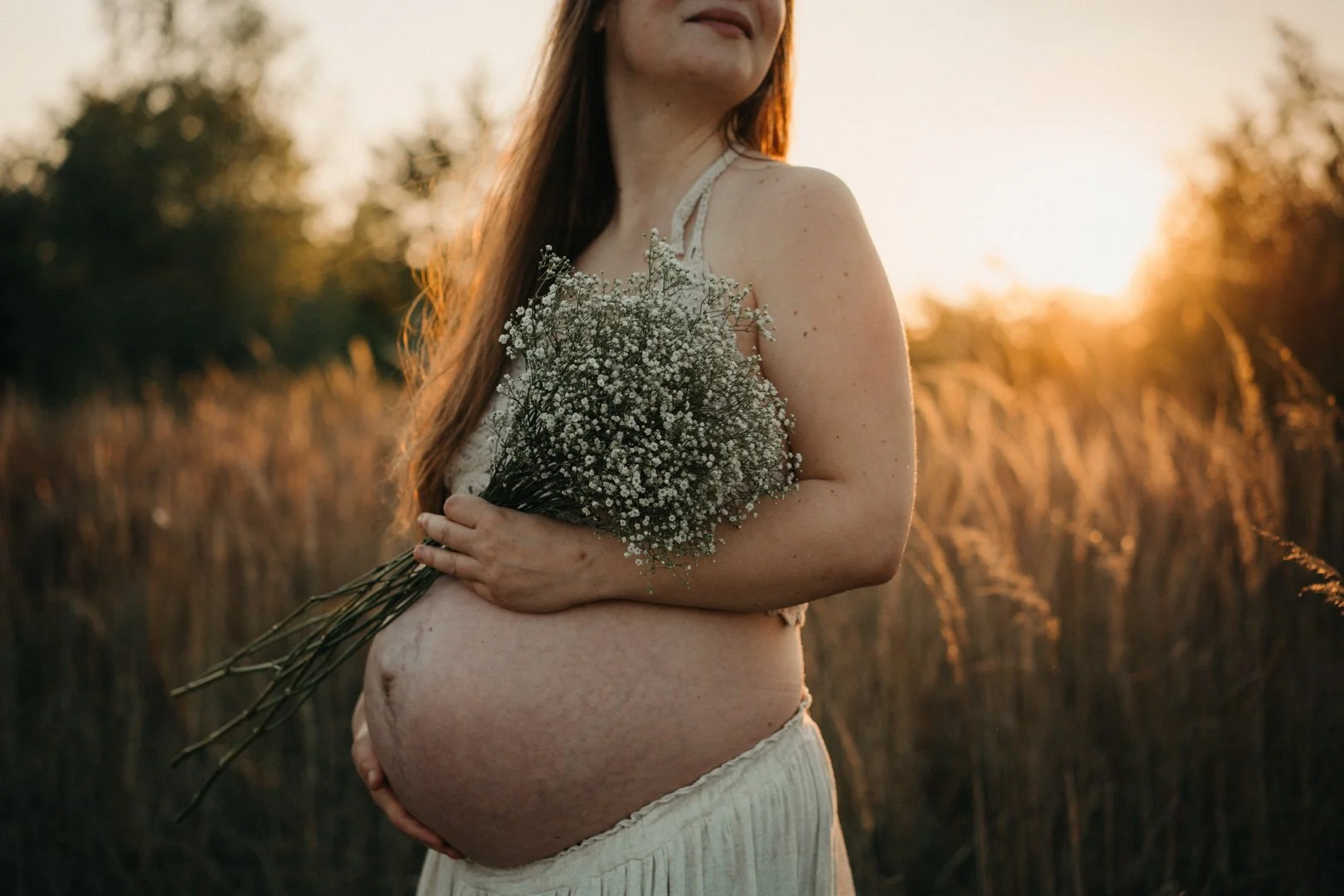 Babybauchshooting einer schwangeren Frau im Sonnenuntergang auf einer Wiese bei Neuss.