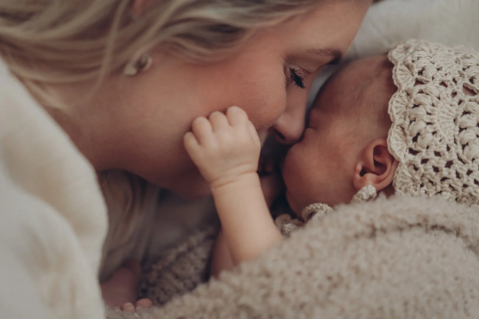 Mama und neugeborenes Baby liegen zusammen im Bett und kuscheln ganz eng miteinander.