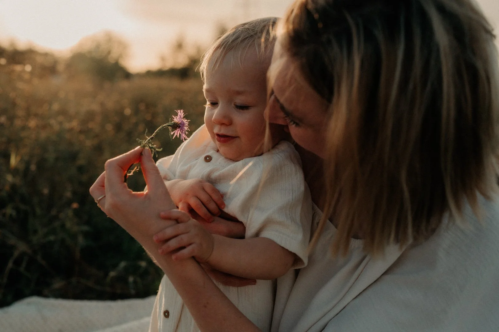 Mama und Baby schauen sich zusammen eine Blume im Abendlicht an.