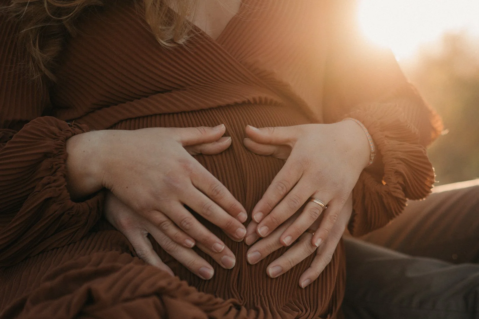Eltern halten Hände auf den Babybauch im Sonnenuntergang.