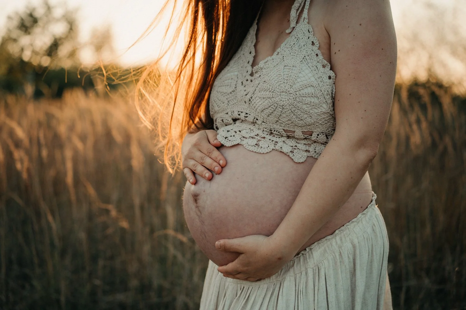 Eine schwangere Frau hält ihren Babybauch im Sonnenuntergang.