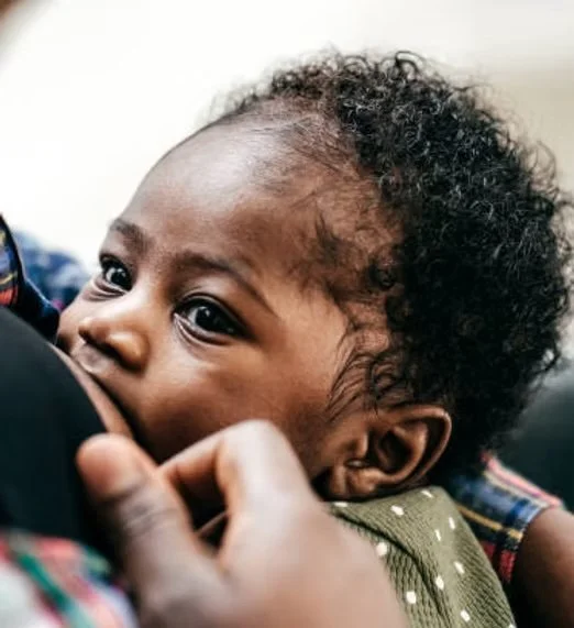 Close-up of a young child with curly black hair and dark skin, resting their head on someone's shoulder.