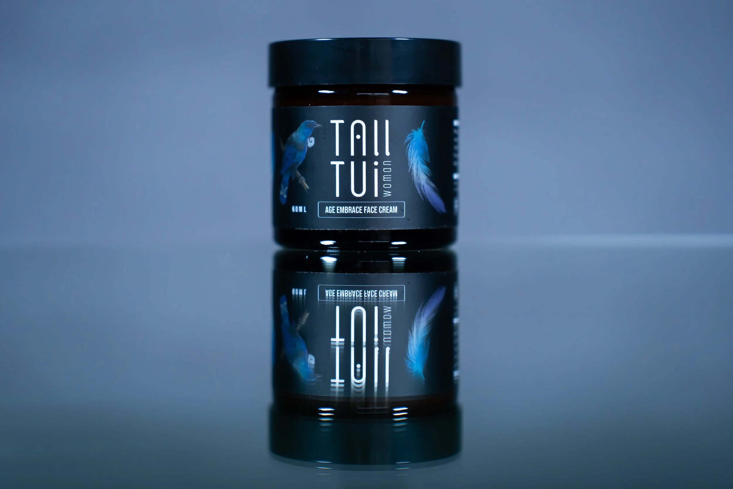 A jar of Tall Tui Age Embrace Face Cream: amber jar, black lid, label with tui bird and feathers