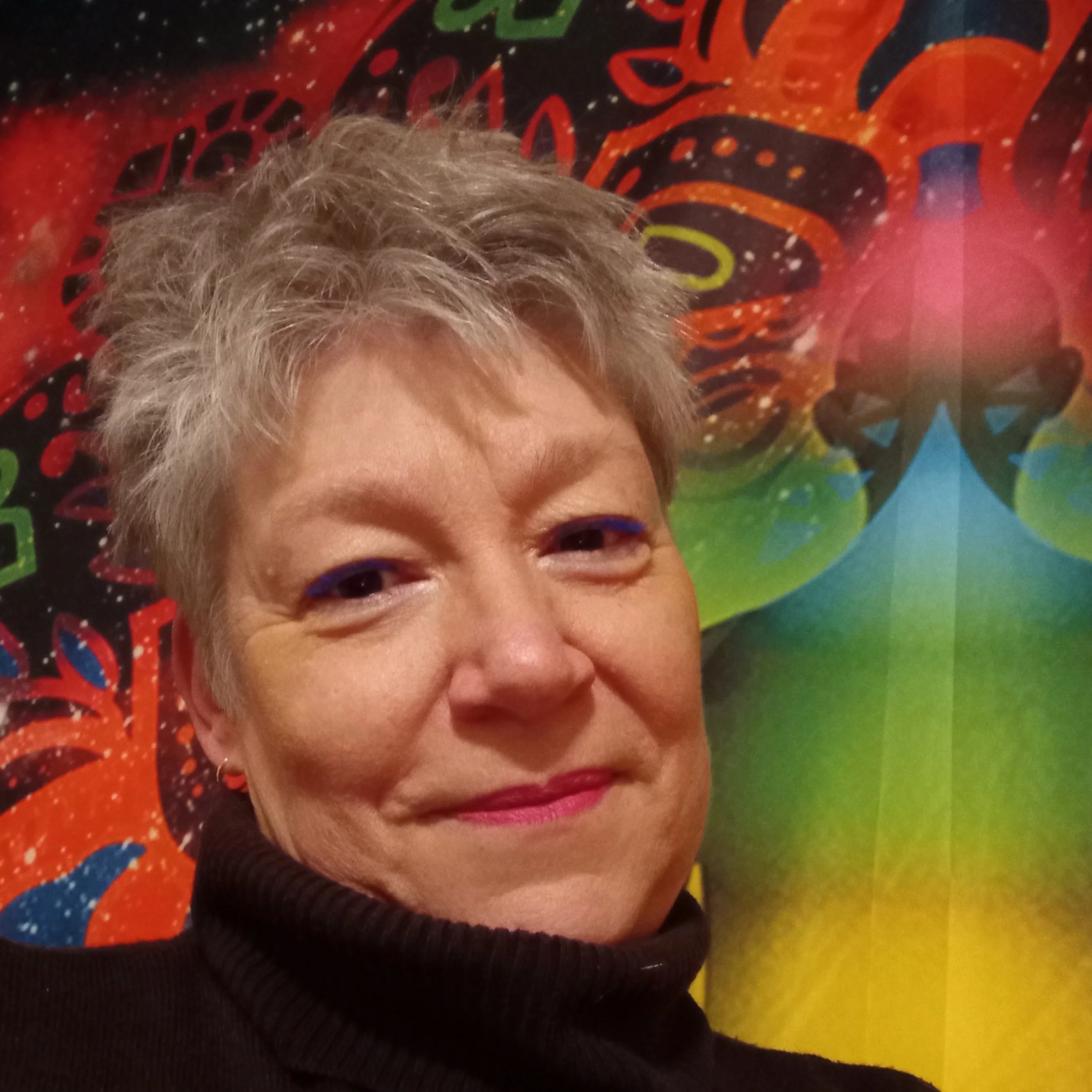 Portrait d'une personne à cheveux gris, portant un hoodie noir, devant un fond coloré avec un motif de papillon artistique