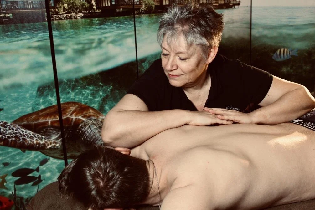 Une femme donne un massage à un homme allongé face contre terre, avec un décor de fond représentant la mer et des poissons.