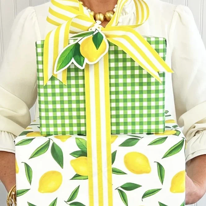 Person holding two wrapped presents with lemon and green leaf patterns, decorated with a yellow and white striped ribbon and bow