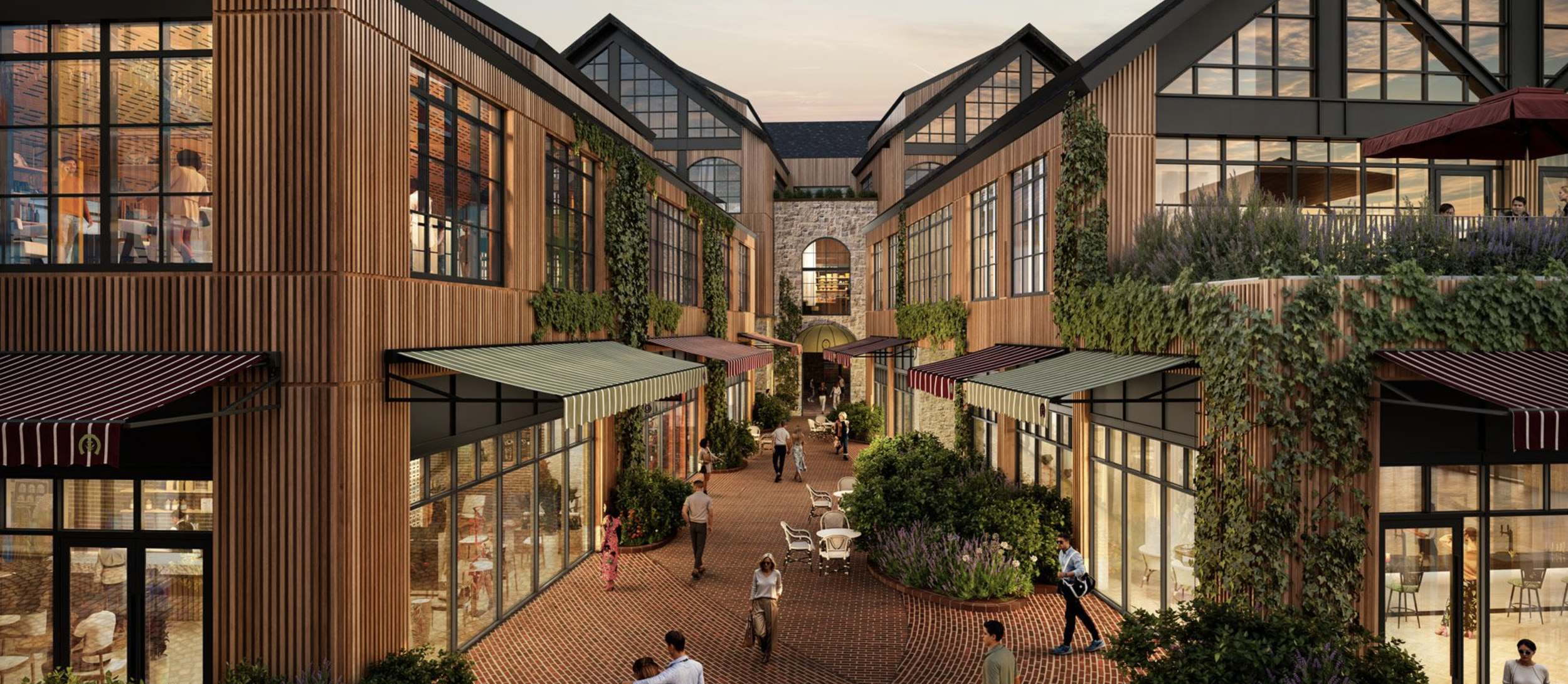 A modern outdoor shopping and dining area with brick pathways, surrounded by multi-story buildings with large windows and wooden paneling, decorated with greenery and awnings, during sunset.