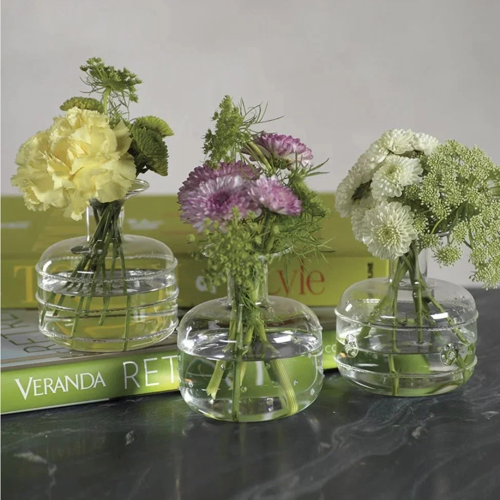Three small glass vases filled with water, each holding a bouquet of flowers, placed on a surface with books in the background.