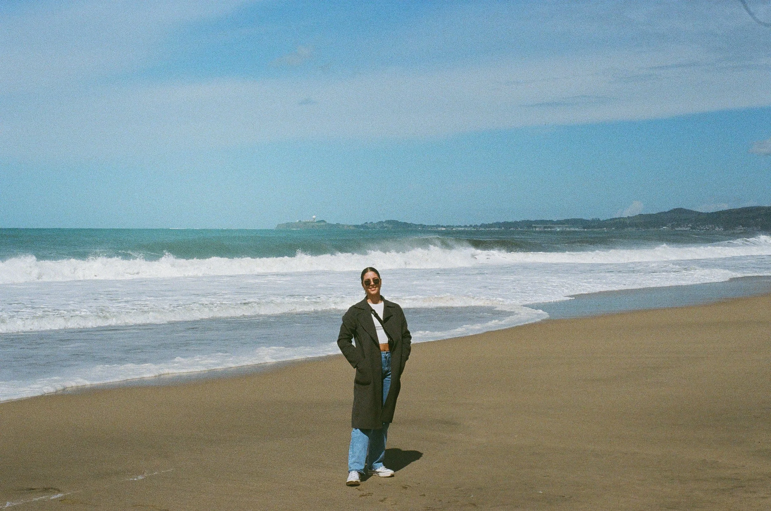 Female therapist in downtown Guelph standing on a beach thinking about couples therapy in Ontario wearing jeans and a long coat