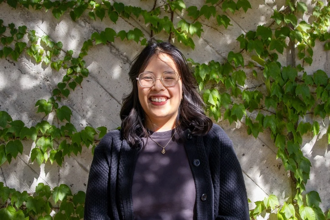 An Asian female therapist in downtown Guelph smiling about grief therapy for teens in Ontario, with leaves and a wall behind her