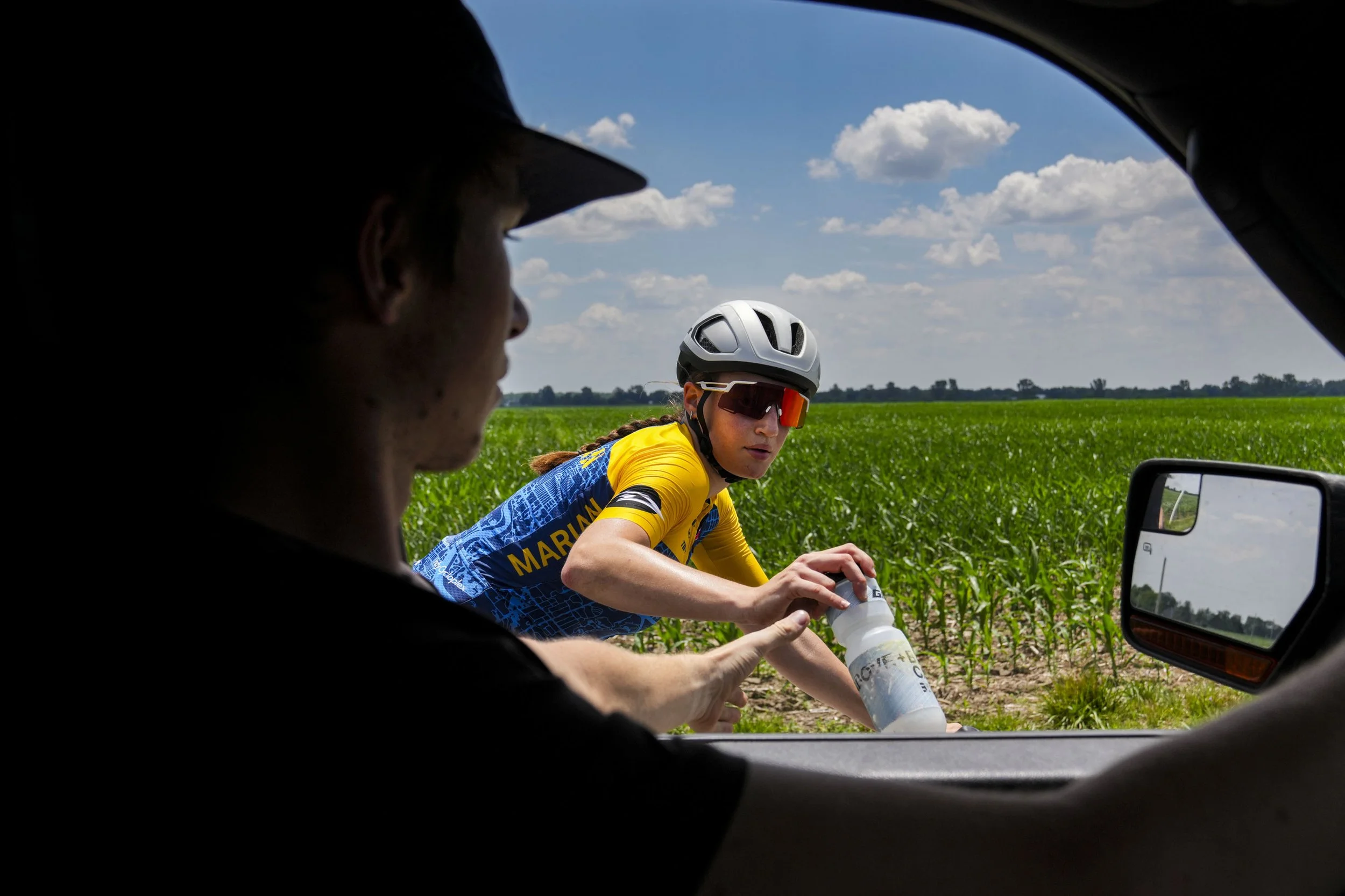 Stephanie Lawrence grabs a water bottle from her boyfriend Fred Meredith during a training session around Indianapolis, Ind., and surrounding towns on Wednesday, July 2, 2025. A 15-hour drive away from the other four pedalers on that quint bike of he