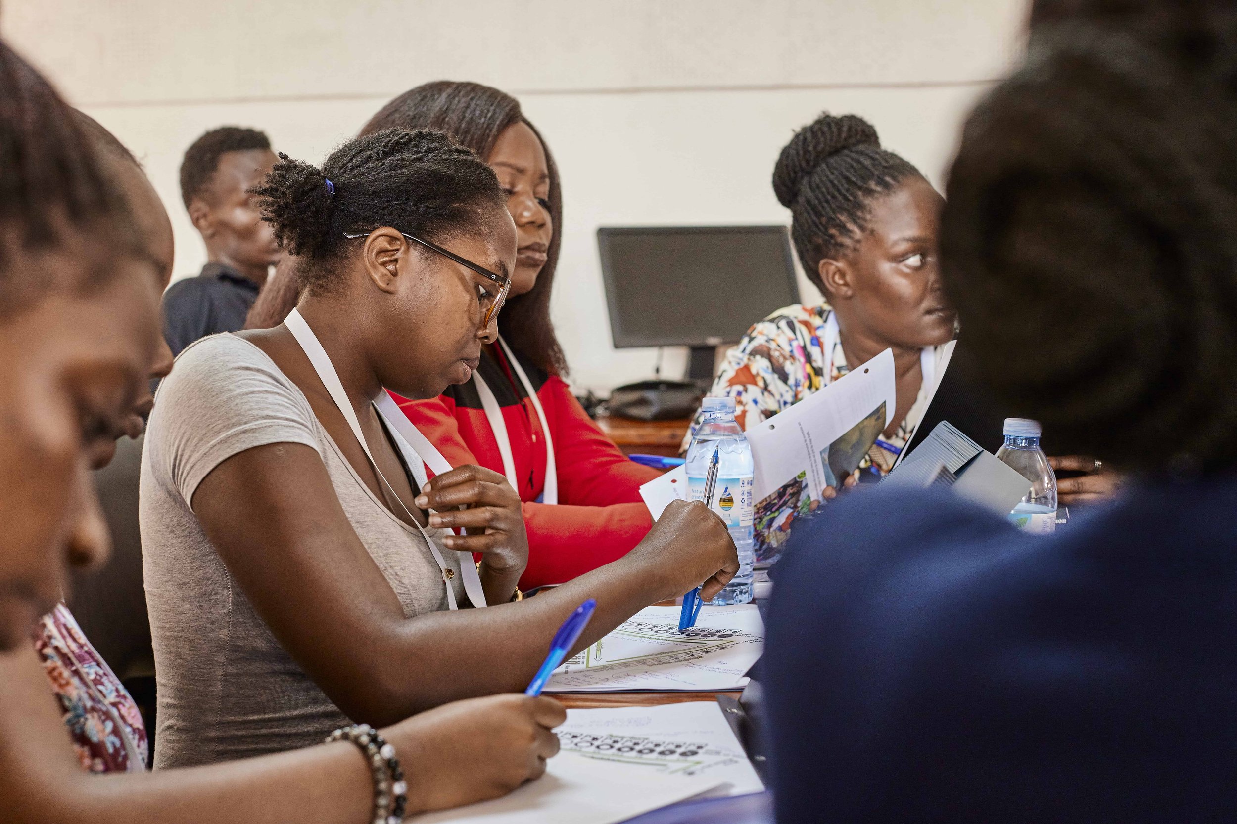 Group of women sitting at a table during a meeting or workshop, reading documents and drinking water.