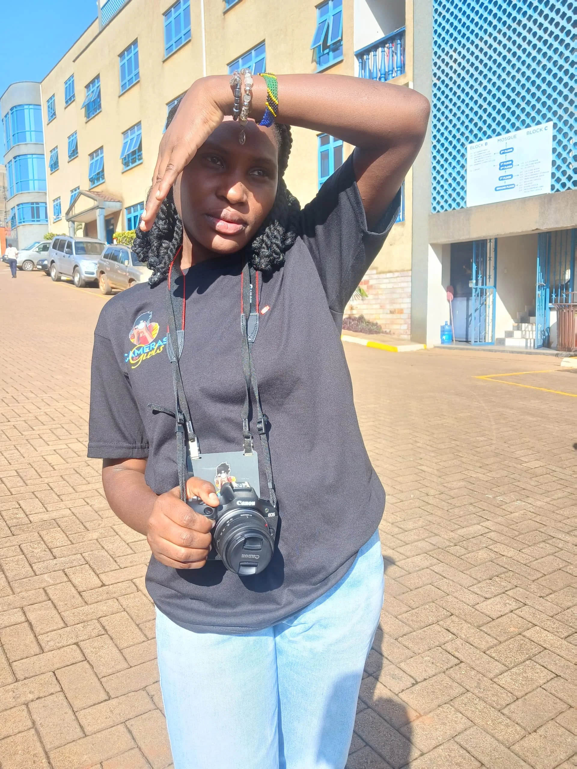Teopista Namuwaya, a student from the 5th cohort in Uganda, stands with her hands blocking the sun, while holding her camera