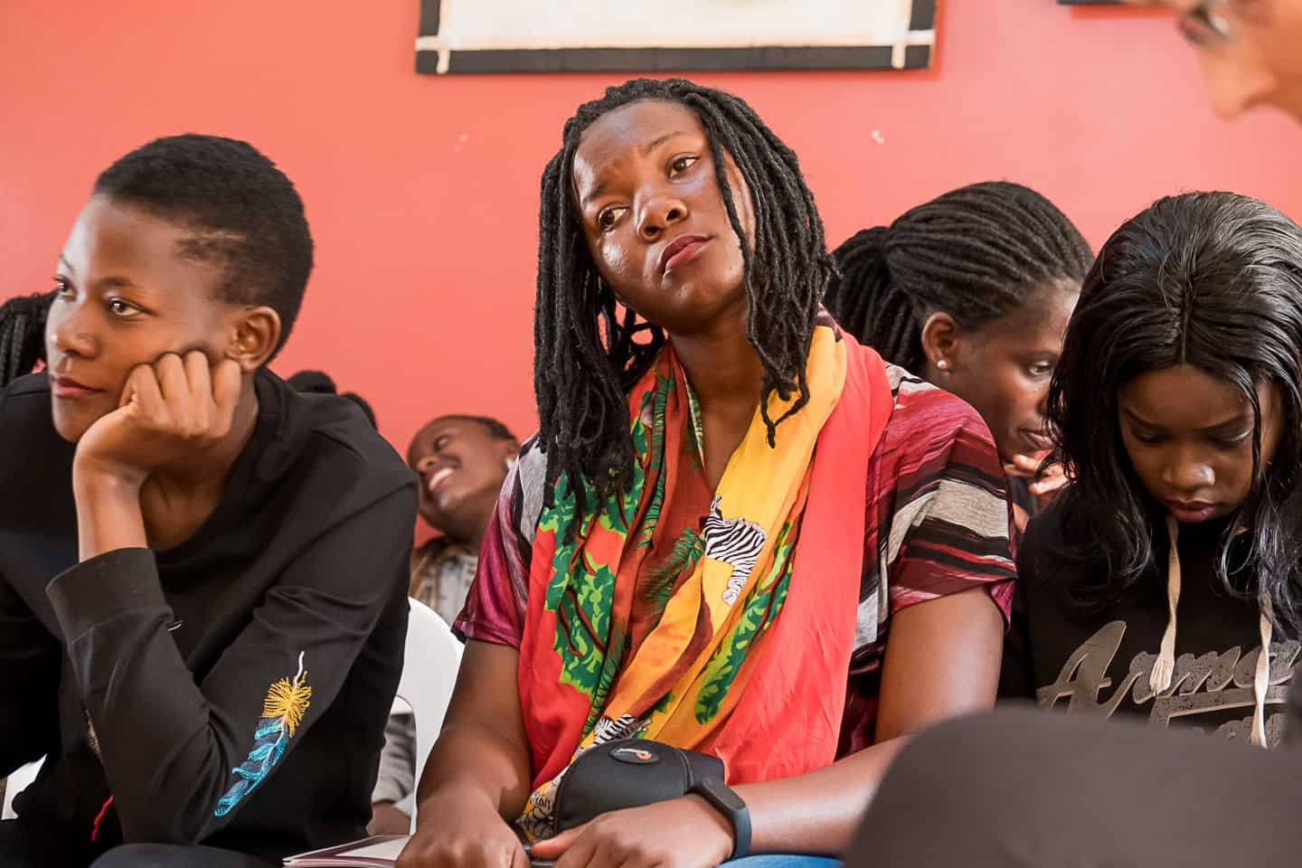 Group of students seated in a classroom, some appear attentive while one girl in the center looks bored or uninterested.