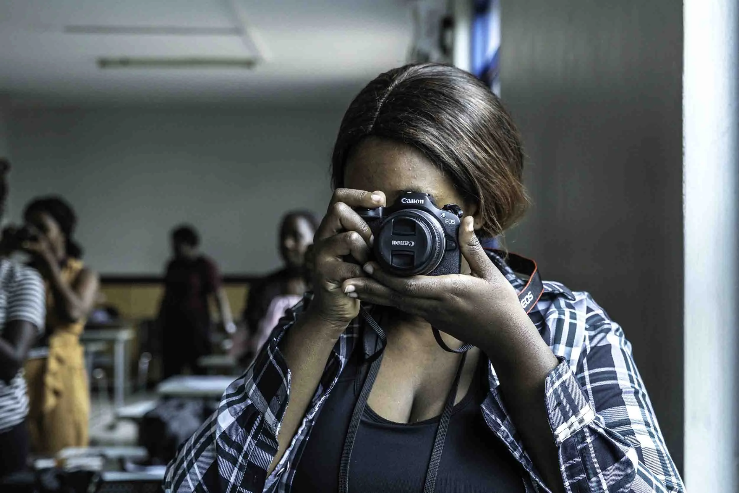 A person taking a photo with a Canon camera in a room filled with other people, some of whom are also taking photos or videos.