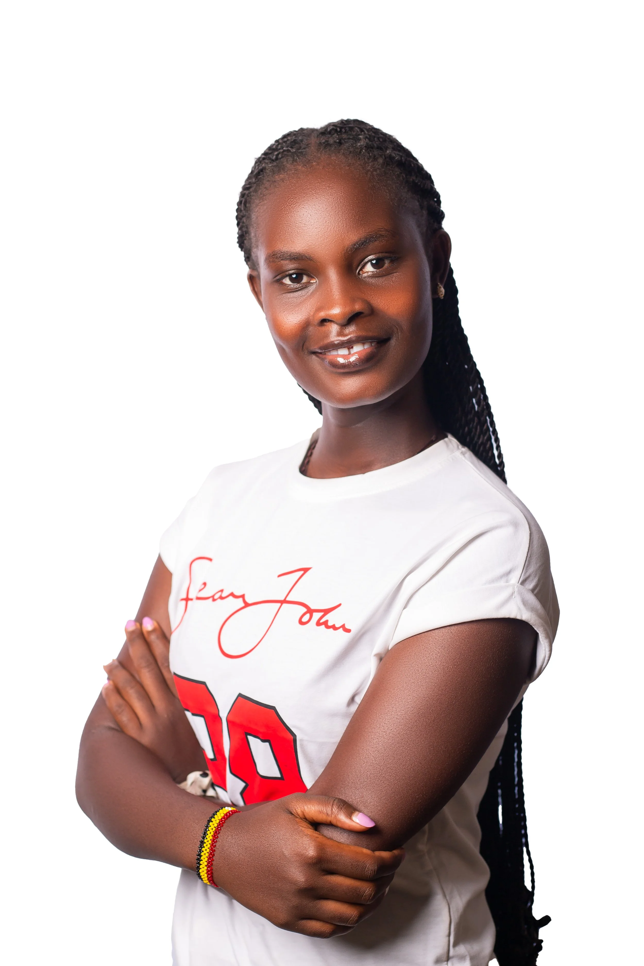 A young woman with dark skin, braided hair, and a bright smile, wearing a white t-shirt with red lettering and a colorful bracelet, standing with arms crossed against a white background.