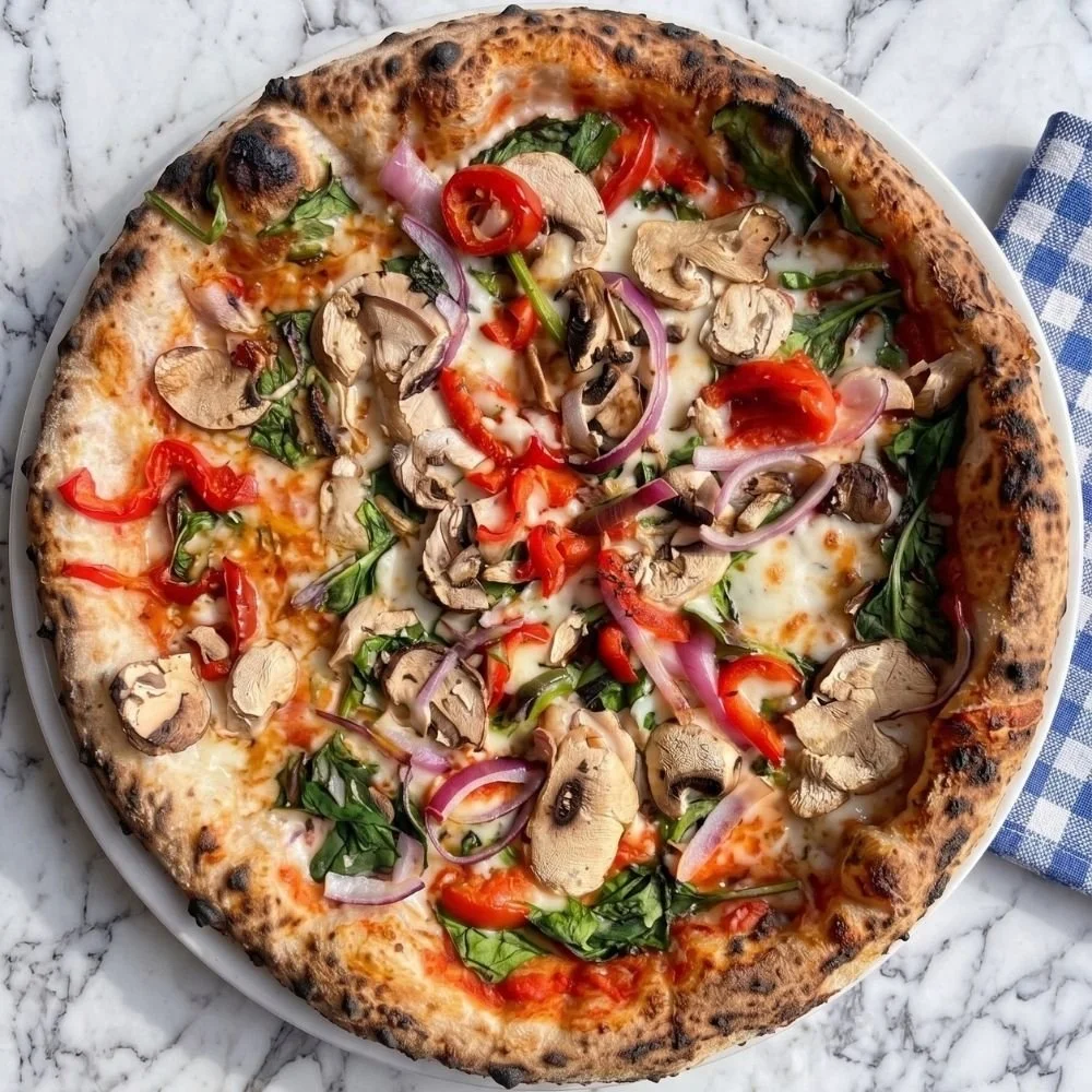 Close-up of a vegetariana pizza with mushrooms, red onions, spinach, and red bell peppers on a white plate.