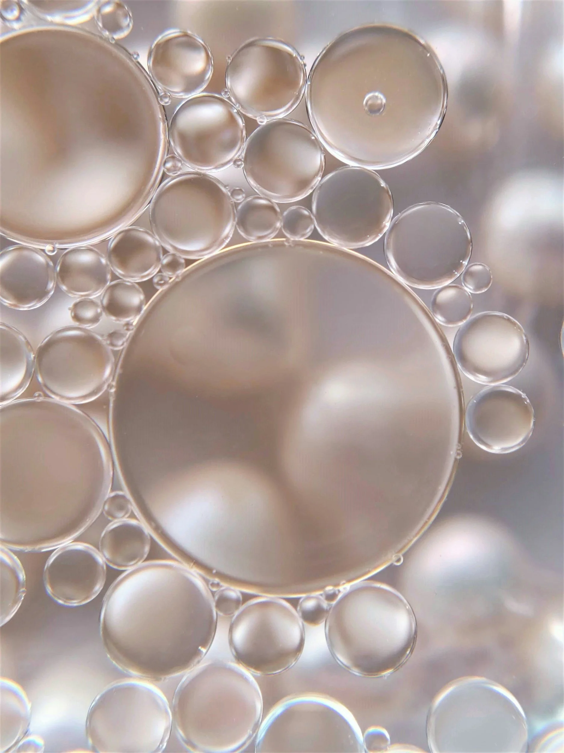 Close-up of bubbles floating in a liquid, varied in size, with a pearlescent or iridescent appearance.