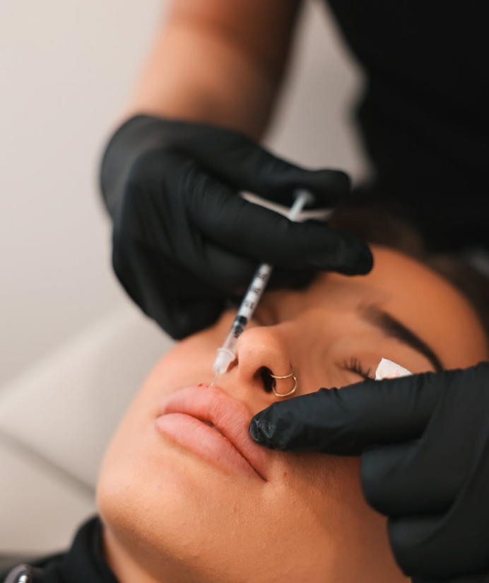 Person receiving a cosmetic injection in the lips from a practitioner wearing black gloves.