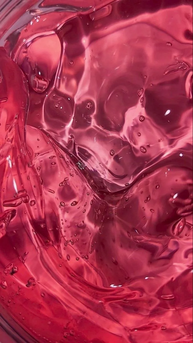 Close-up of swirling red liquid with bubbles and reflections, resembling wine or similar beverage.