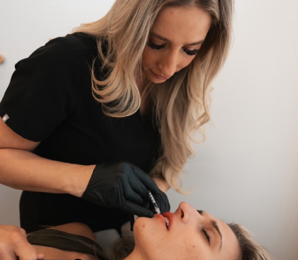 A woman wearing black gloves applying lip makeup to a woman lying down