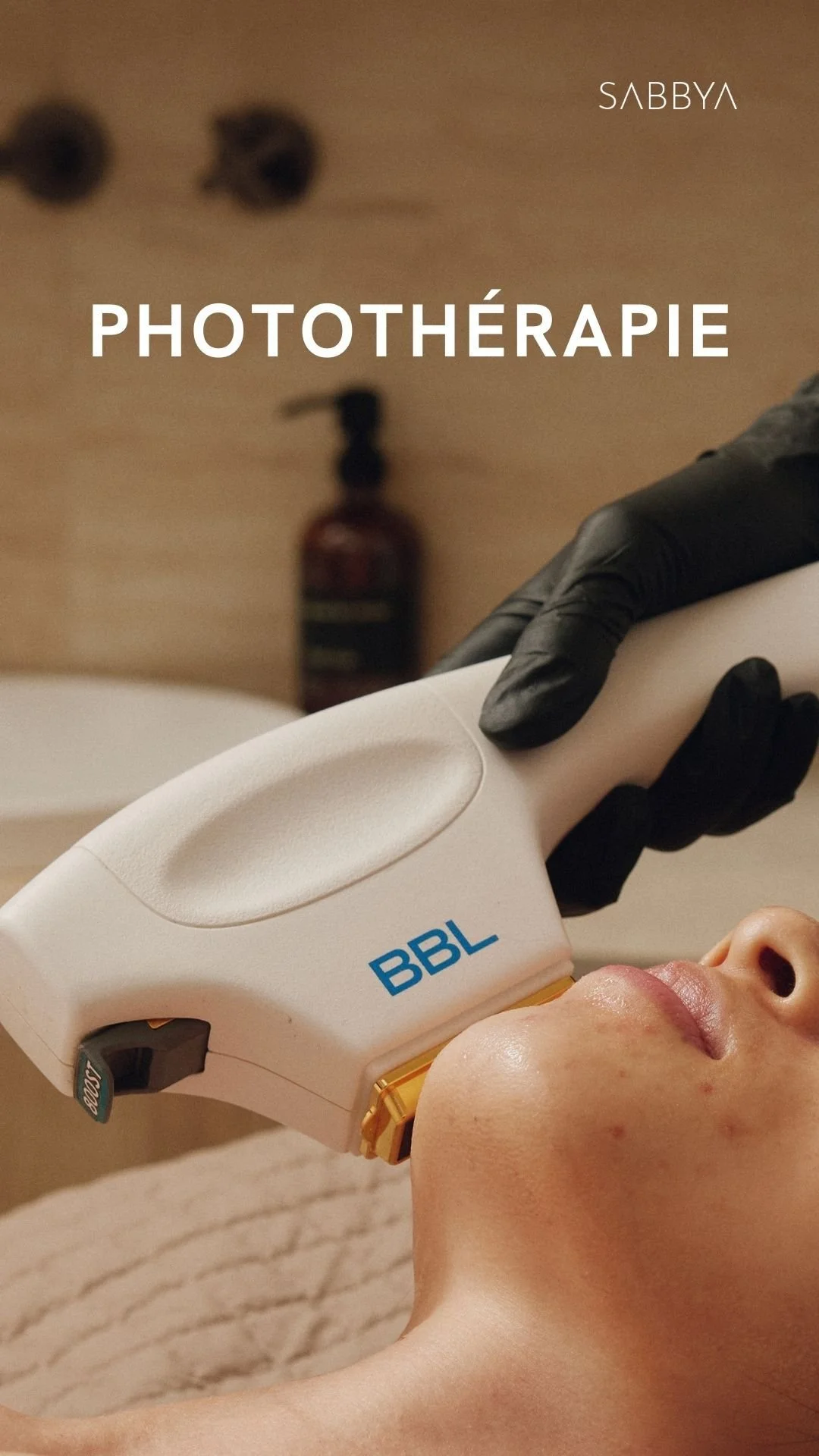A person receiving phototherapy treatment on their face with a handheld device labeled BBL, wearing a beige top, in a clinical setting.
