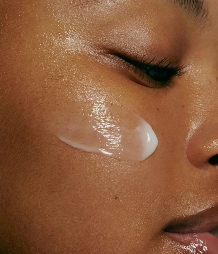 Close-up of a person’s face with a dollop of white cream or lotion on their cheek, near the eye.