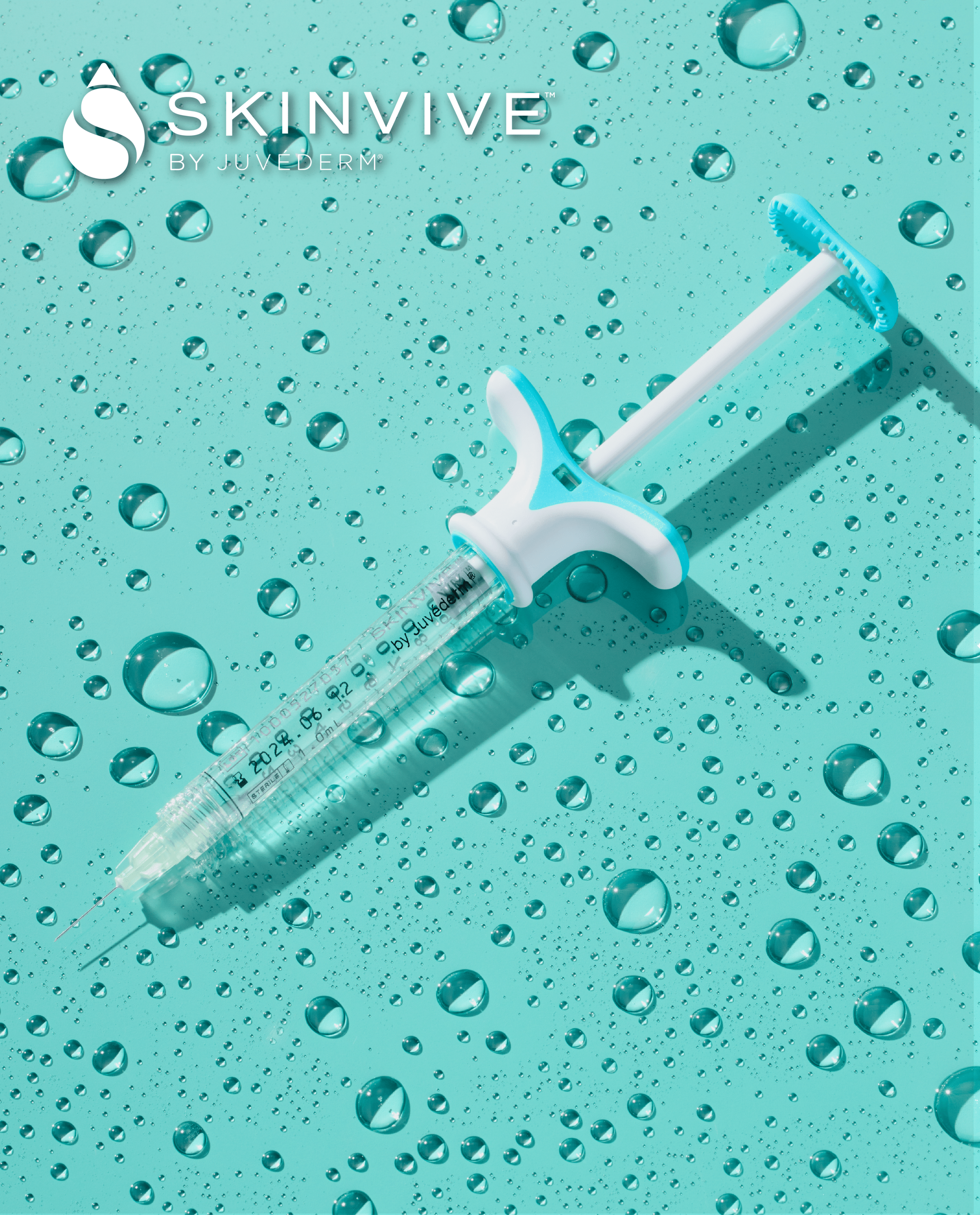 A medical syringe with a white and blue handle and a clear barrel, lying on a turquoise surface with water droplets scattered around.