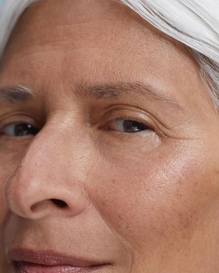 Close-up of a mature person's face with silver hair, focusing on one eye winking and visible skin details.