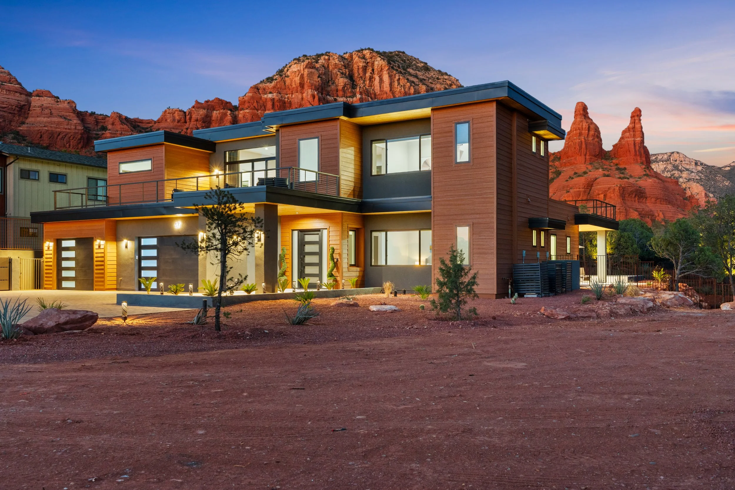 Modern two-story house with large windows and balconies, set against red rocky mountains during sunset. Modern, luxury home in Scottsdale, AZ