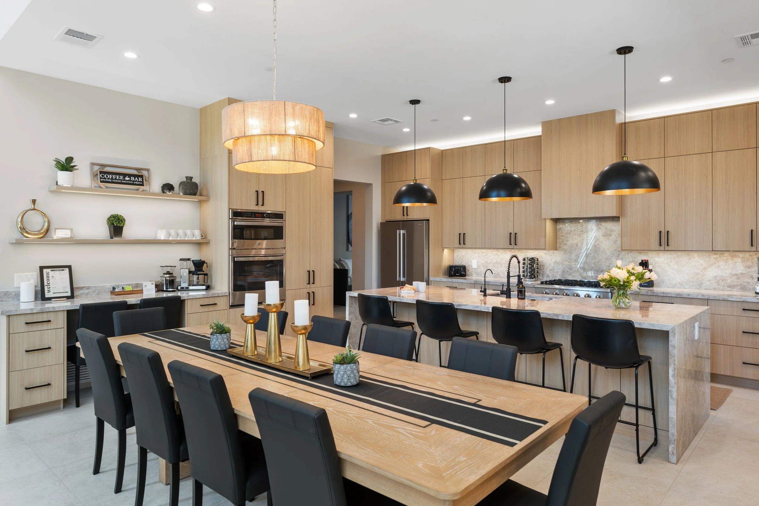 Modern kitchen with wooden cabinets, black pendant lights, a large dining table with black chairs, and decorative items on shelves. Luxury home in Sedona, AZ