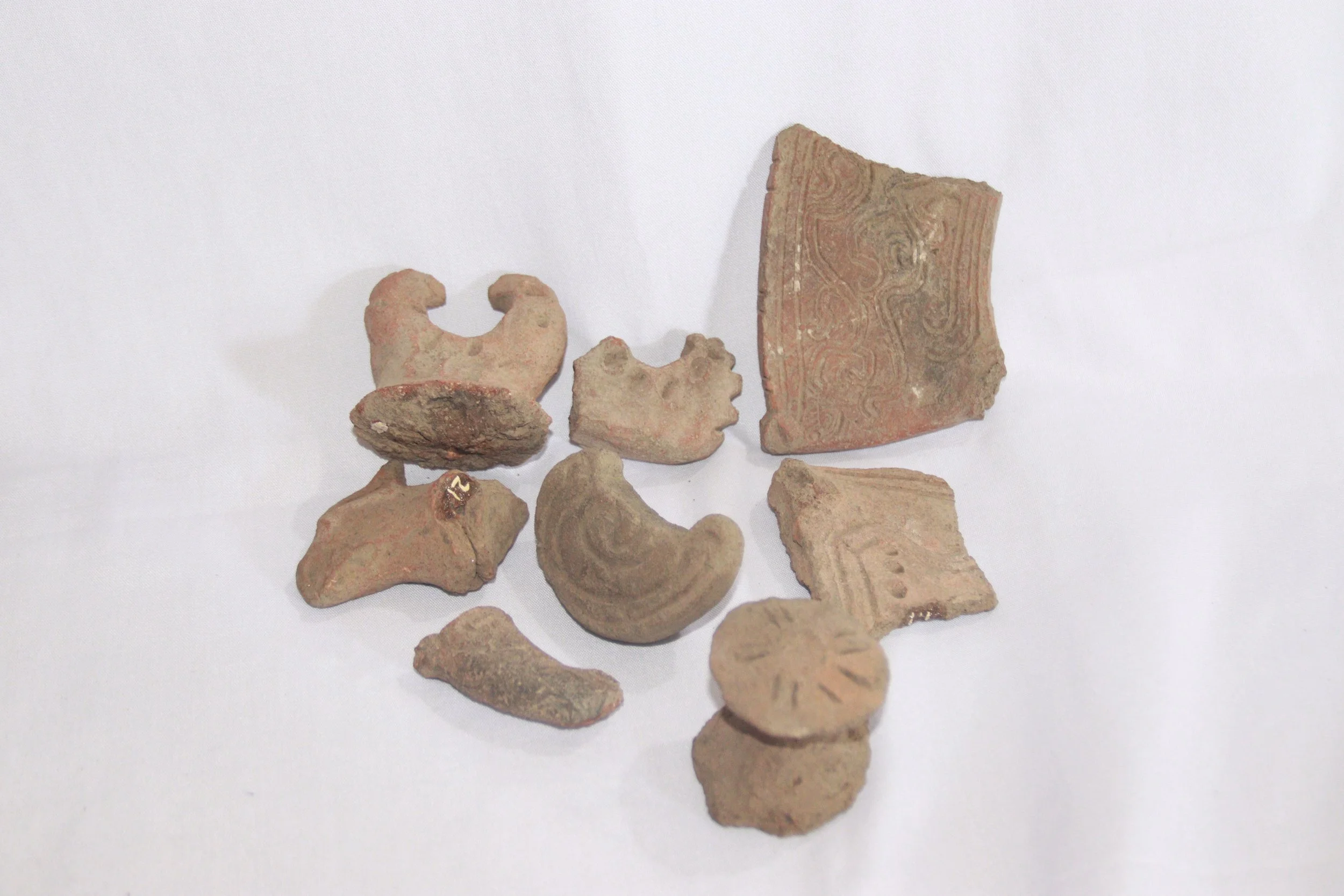 archive number: r-1-022
object reference: 
Pottery fragments
origin: Banda
date: -
notes: Many of these pottery pieces are shaped like bird heads and ears, usually used as handles on clay vessels. On the pottery fragments we can see decorative patter