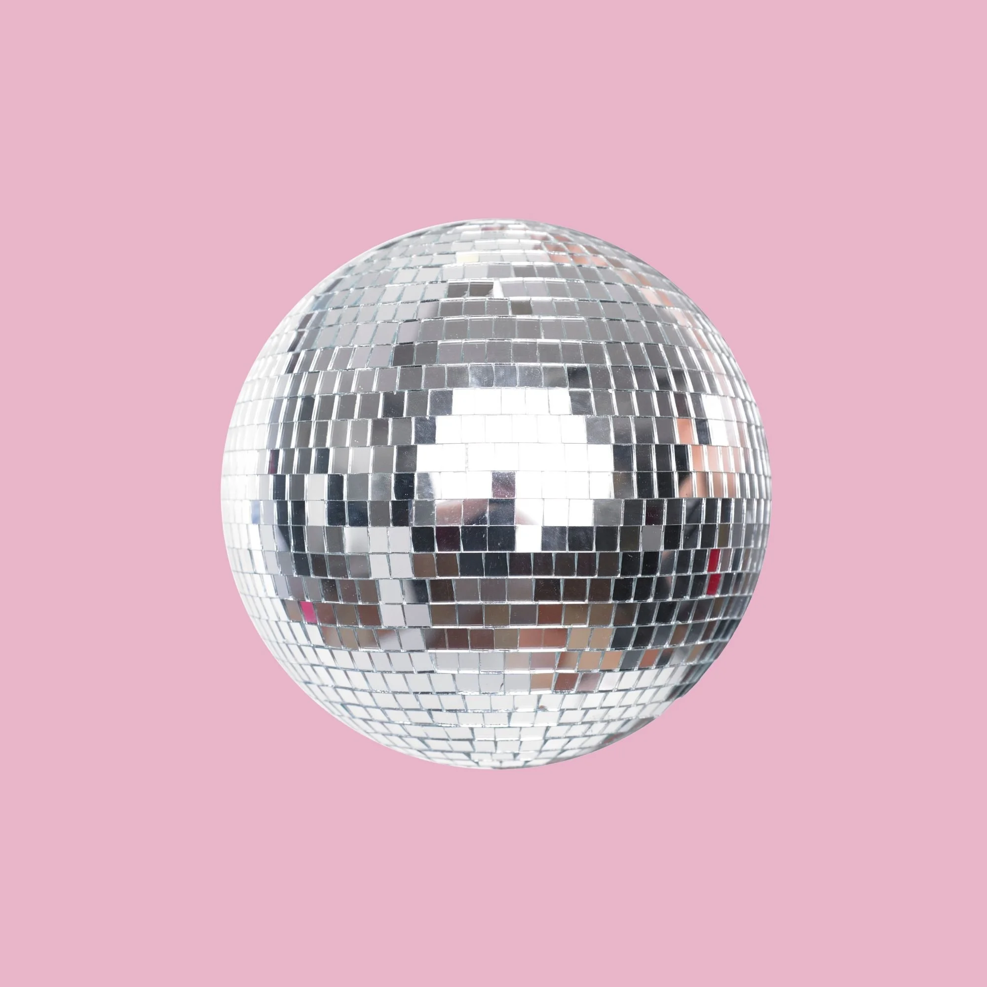 A shiny disco ball with small mirrored tiles reflecting light, set against a pink background.