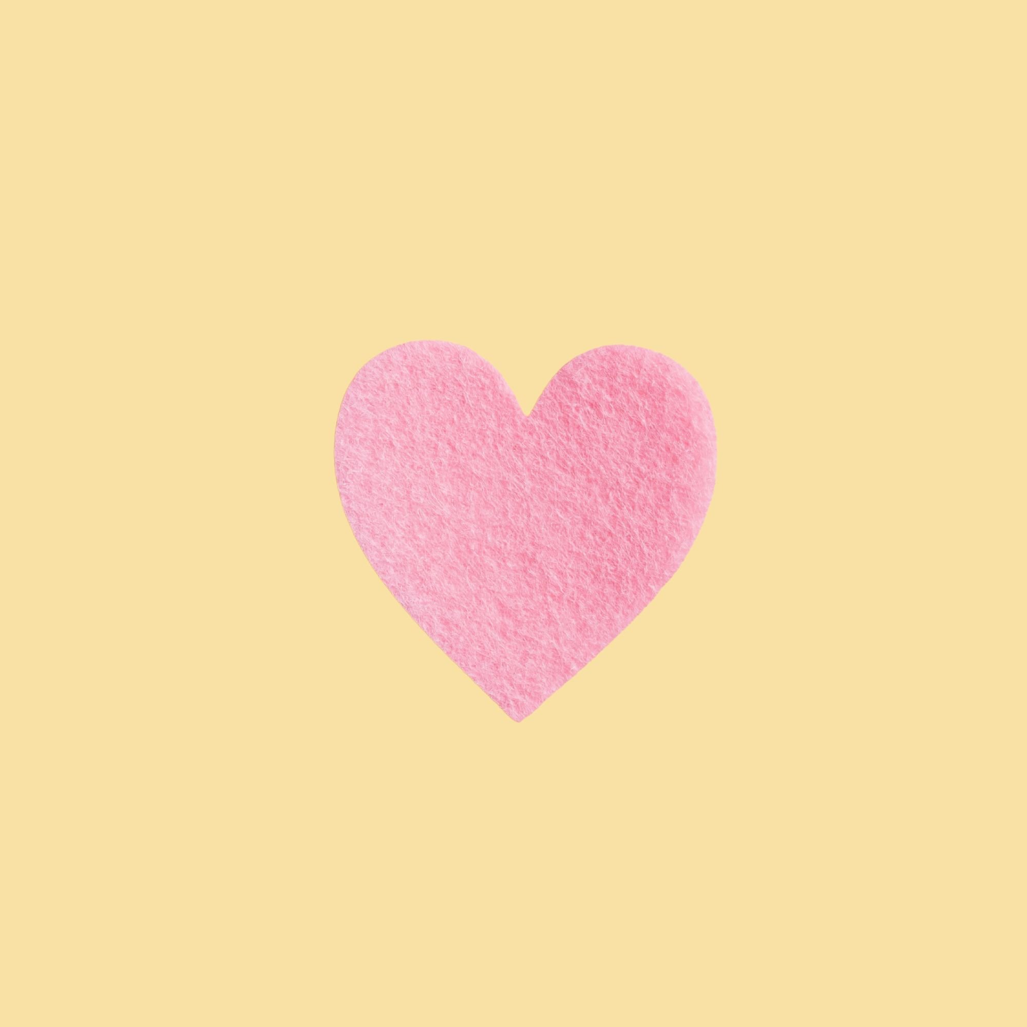 Pink felt heart on a light yellow background.