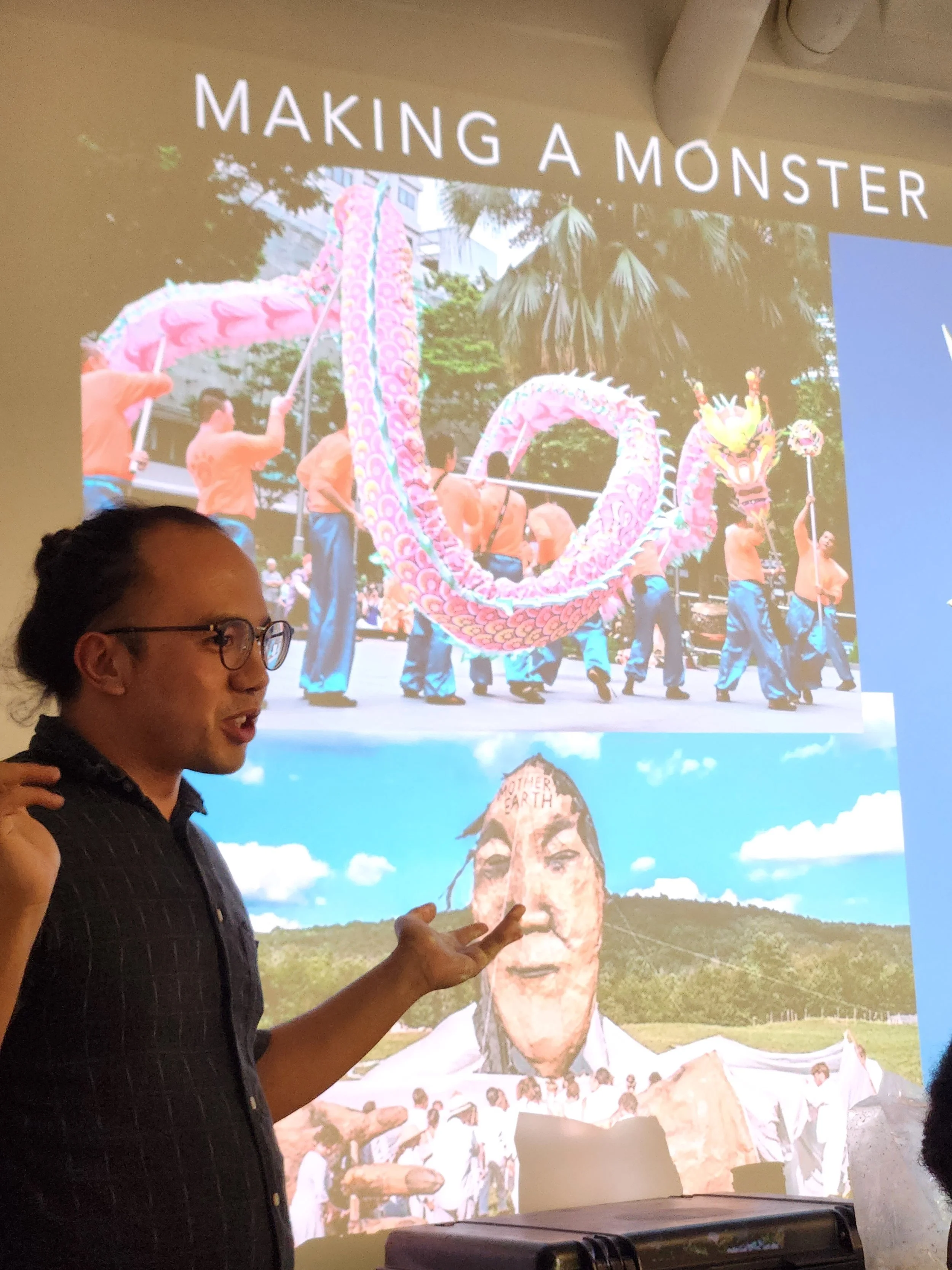 Shanhuan in front of a slideshow depicting various large scale puppets.