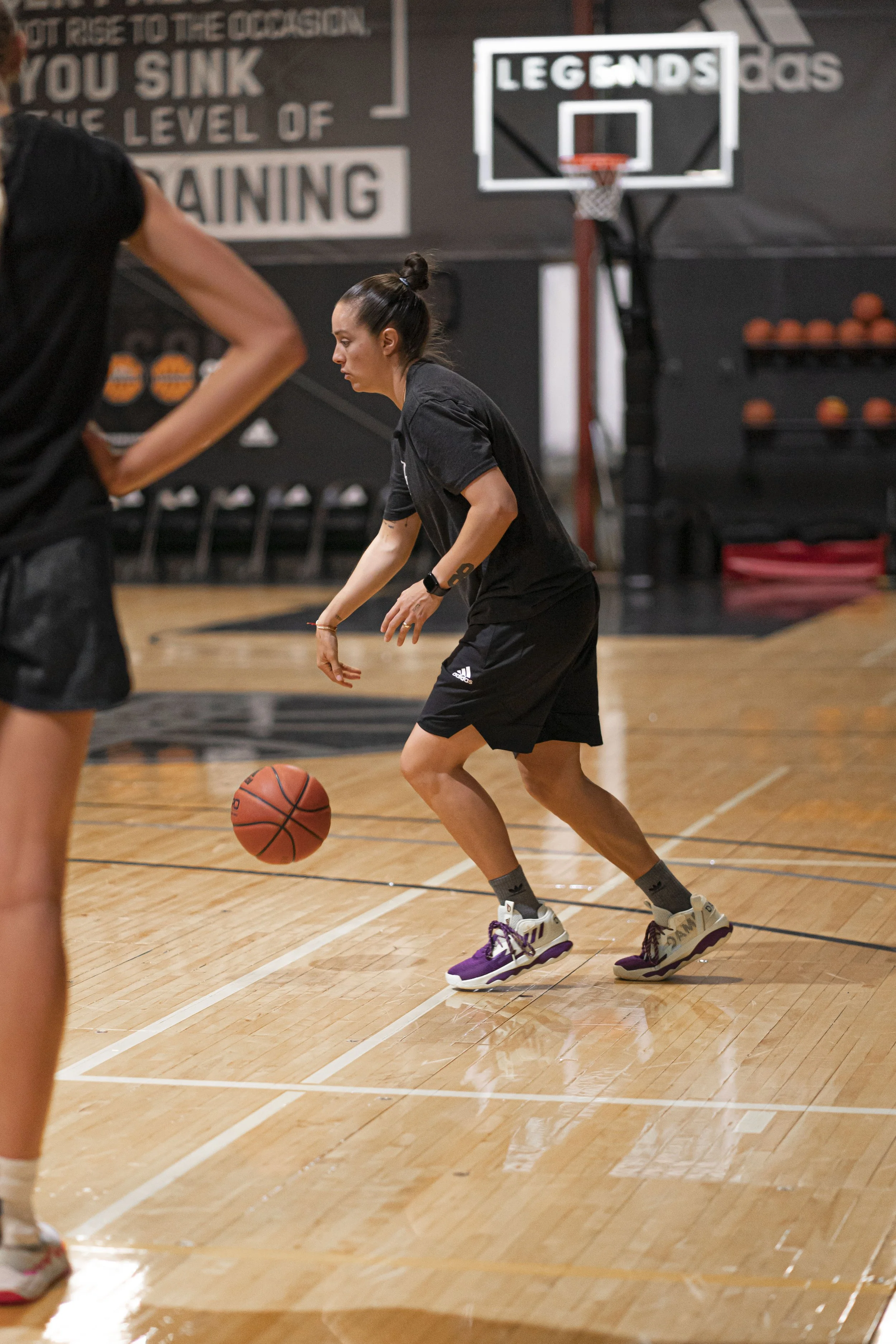 A woman playing basketball dribbling on an indoor court with a basketball hoop in the background.