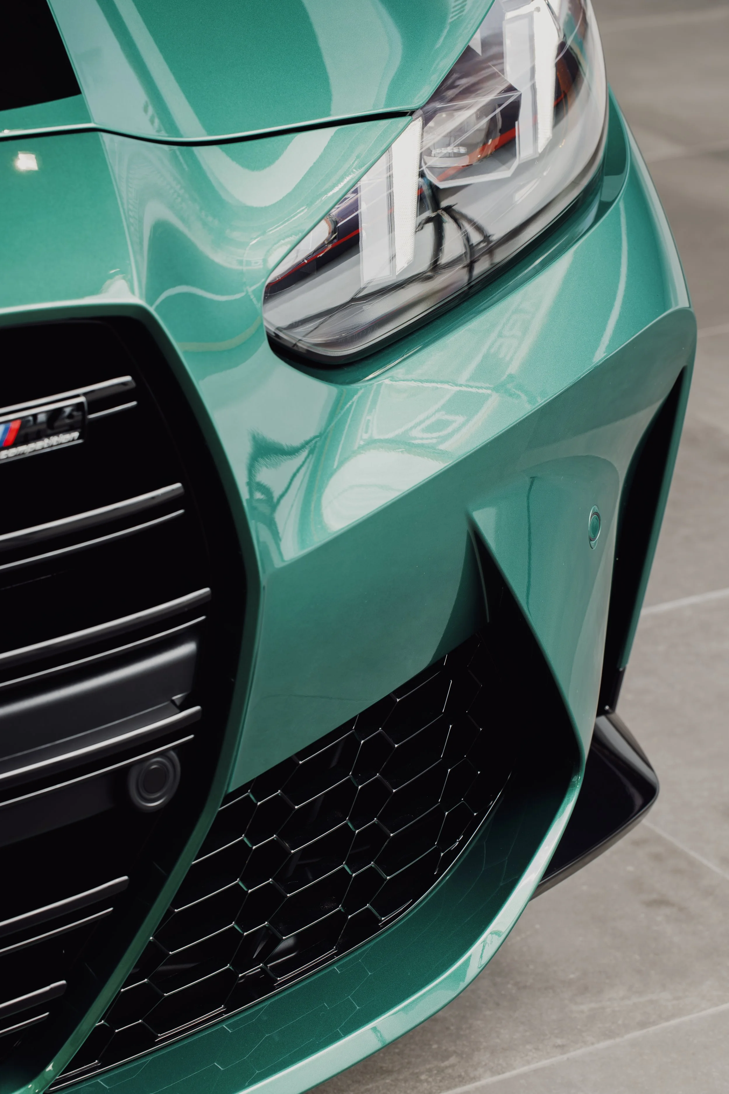 Close-up of the front of a green sports car, showing the headlight, grille, and front bumper.