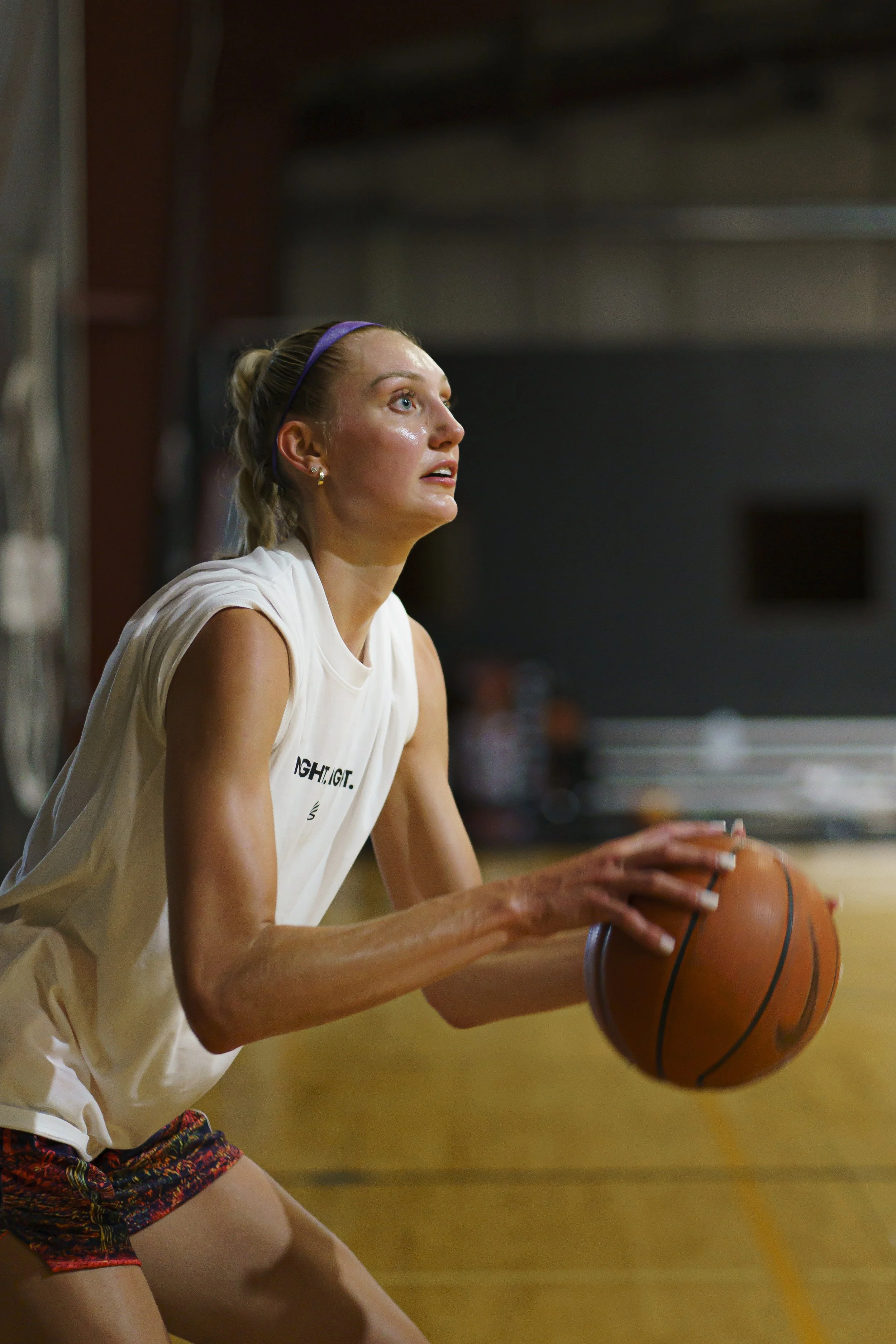 A young woman playing basketball on an indoor court, wearing a white sleeveless top and colorful shorts, holding a basketball with both hands. Cameron Brink. WNBA. Stanford.