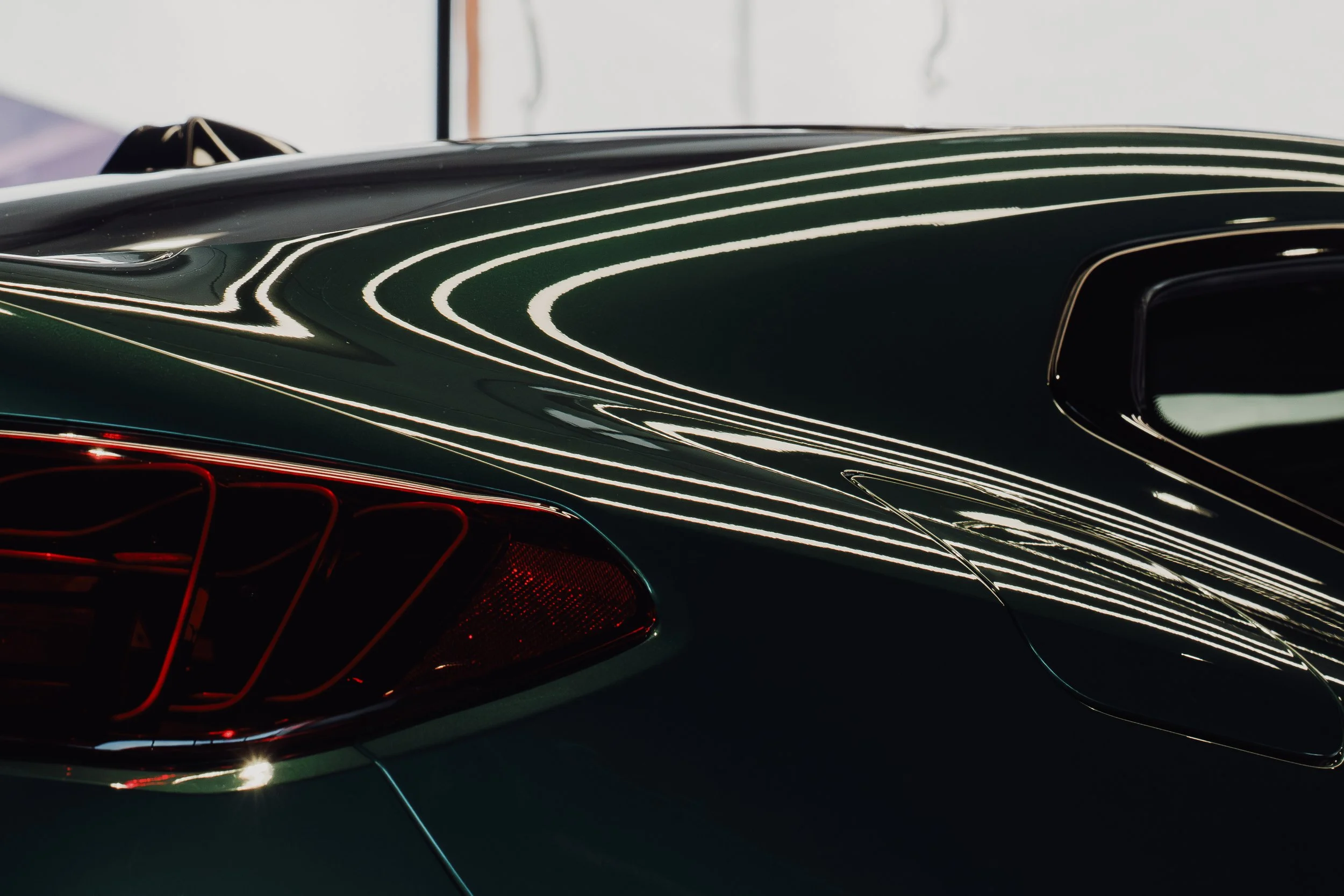 Close-up of a sleek, dark green sports car with bright white and red reflections and a futuristic design, emphasizing the curves and the tail light.