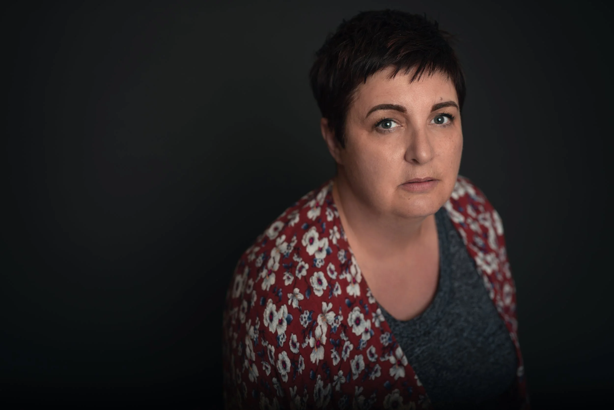 Portrait of a woman with short dark hair wearing a dark top and a red floral shawl against a black background.