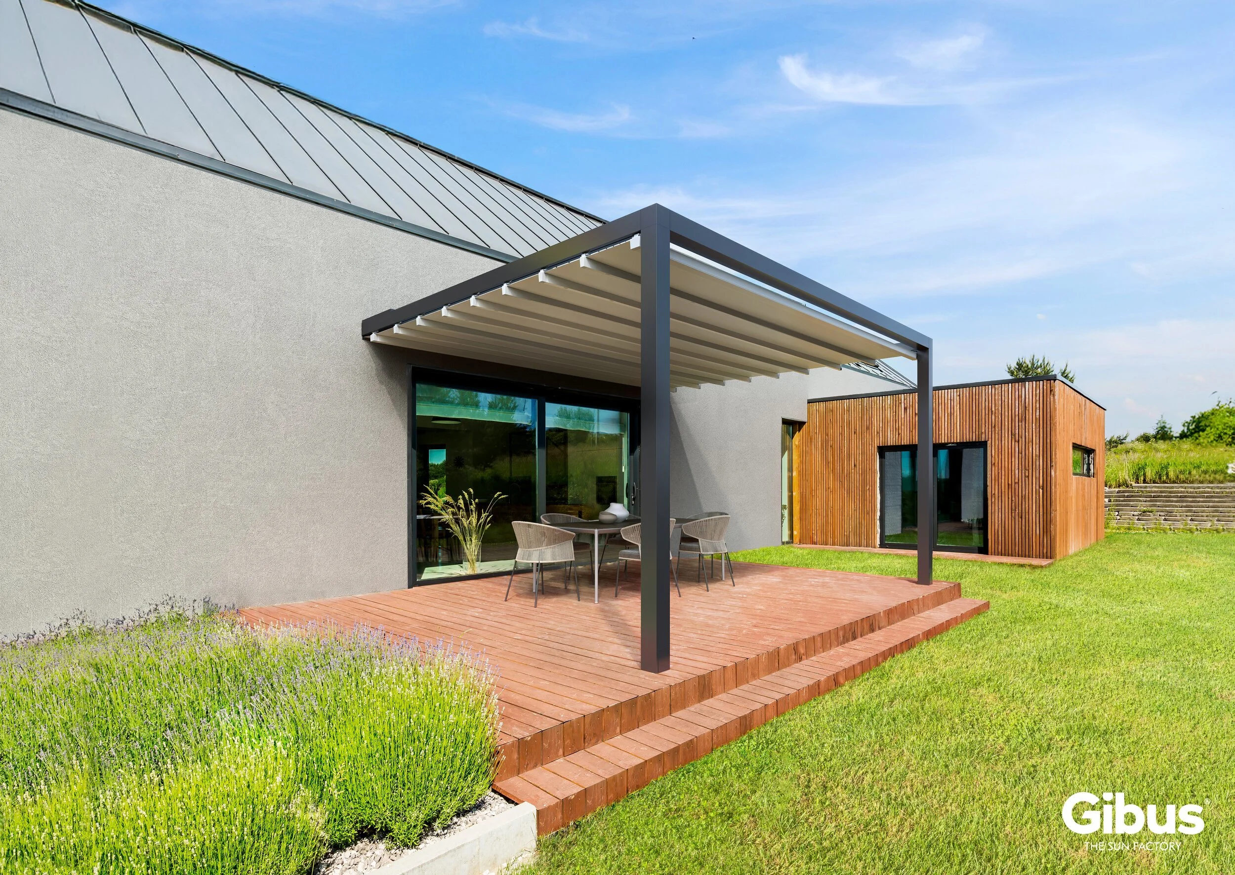 Moderni talo pihalla, jossa terassi varjoisan pergolan alla, puurakenteinen irtoterassi ja vihreä nurmikko.