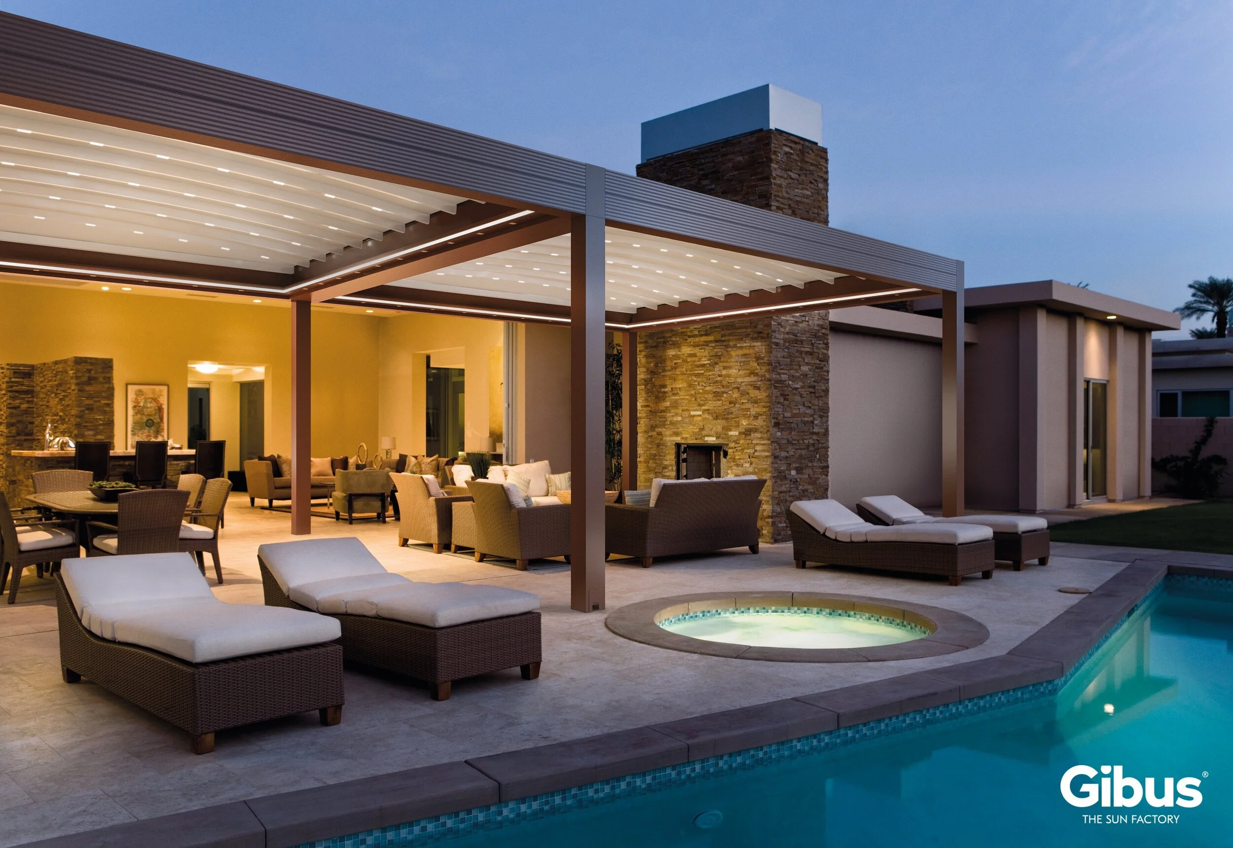 Uima-allasalue iltahämärässä, ulkouima-allas ja poreallas, aurinkovuoteita ja vilttiä, katetut oleskelualuemökit, moderneja rakennuksia, Gibus-brändi logo alhaalla oikealla.