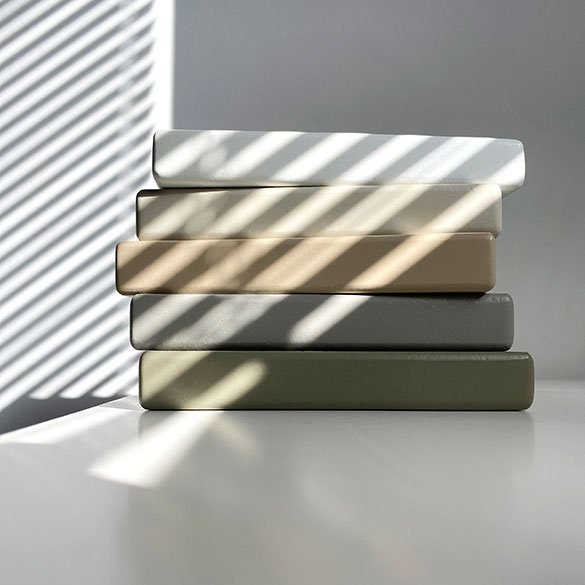 Neljä värilautaa, jotka ovat valkoisesta mustaan, lavastettu ikkunan varjostuksen alla, heijastukset ja varjot peilaten niiden pinnalla.