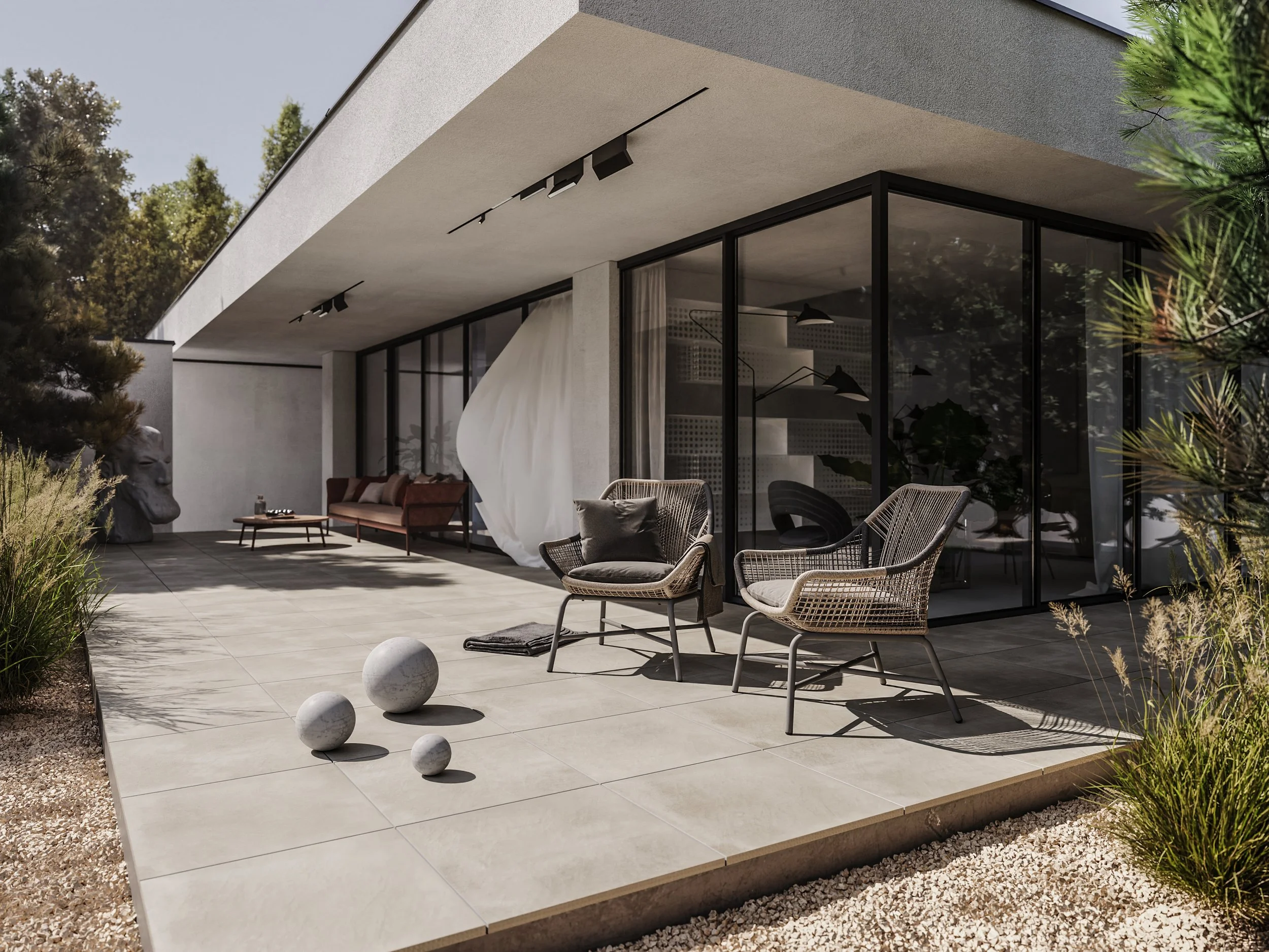 Modernin kivitalon terassi, jossa on ruokapöytä ja kaksi tuolia, sekä tyynyllä varustettu sohvaryhmä, suuret lasi-ikkunat ja puutarhakasveja.