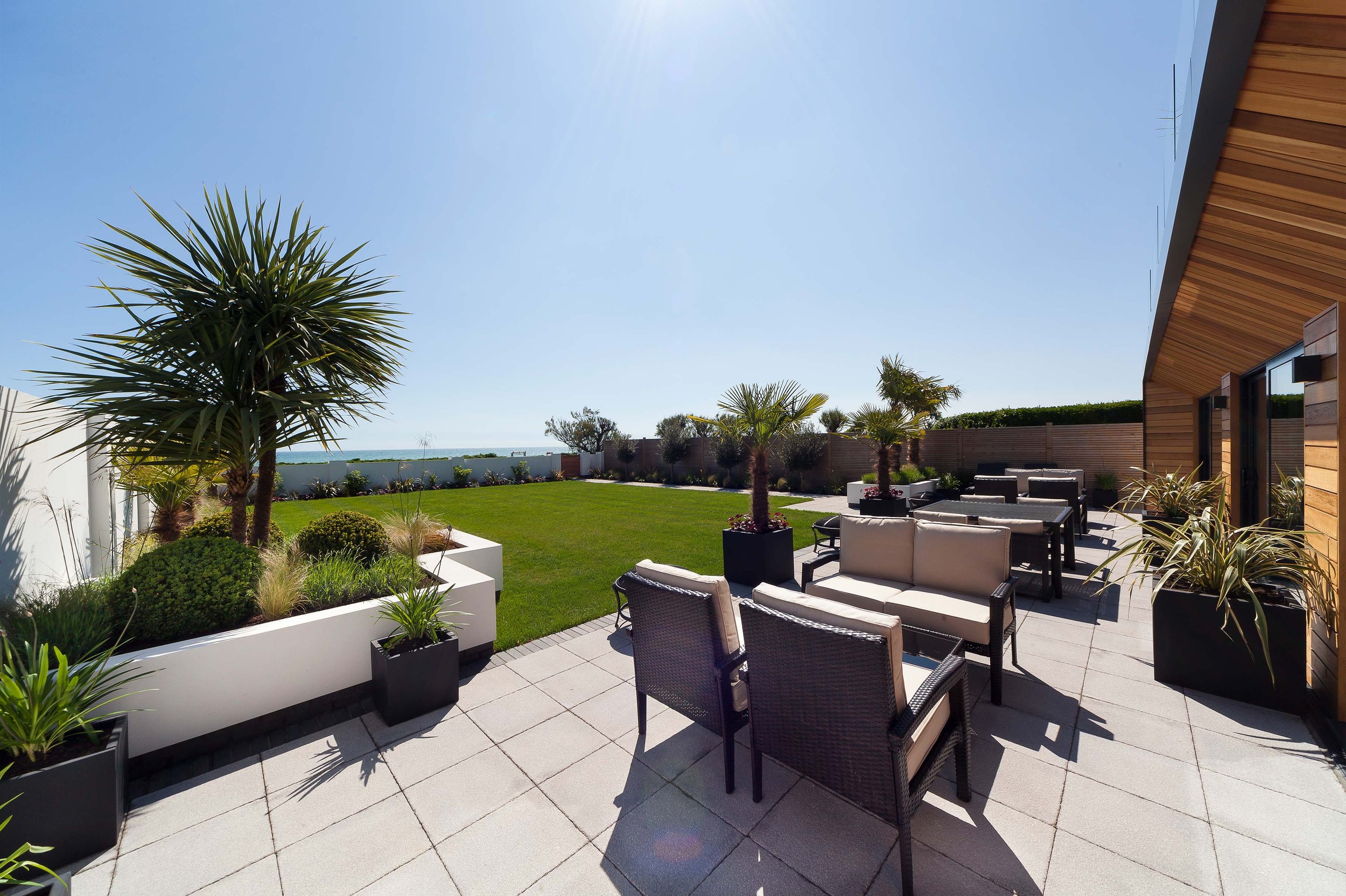 Modern outdoor patio with wicker furniture, palm trees, and well-maintained lawn.