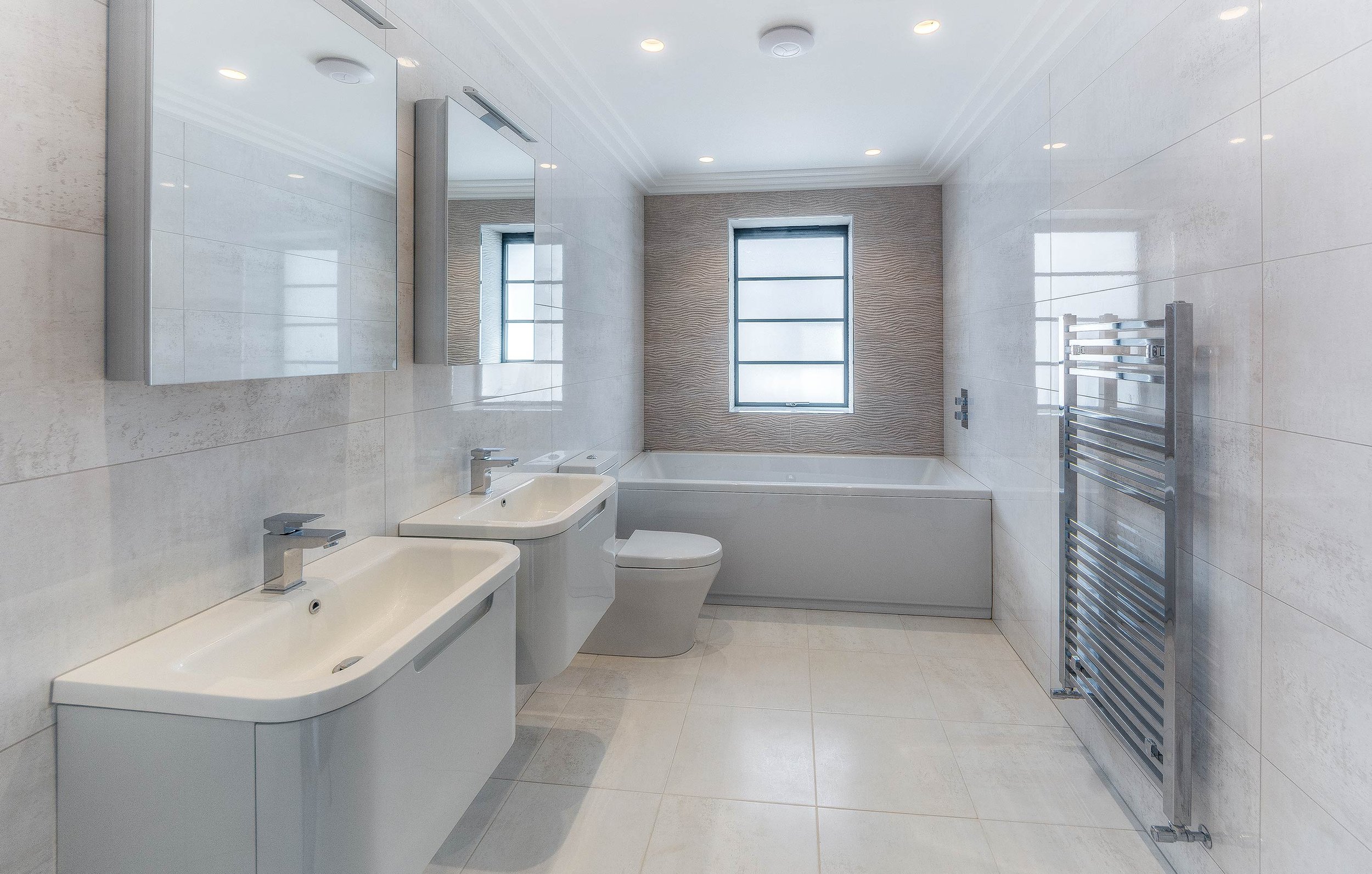 Modern bathroom with dual sinks, toilet, bathtub, mirrors, and heated towel rail.