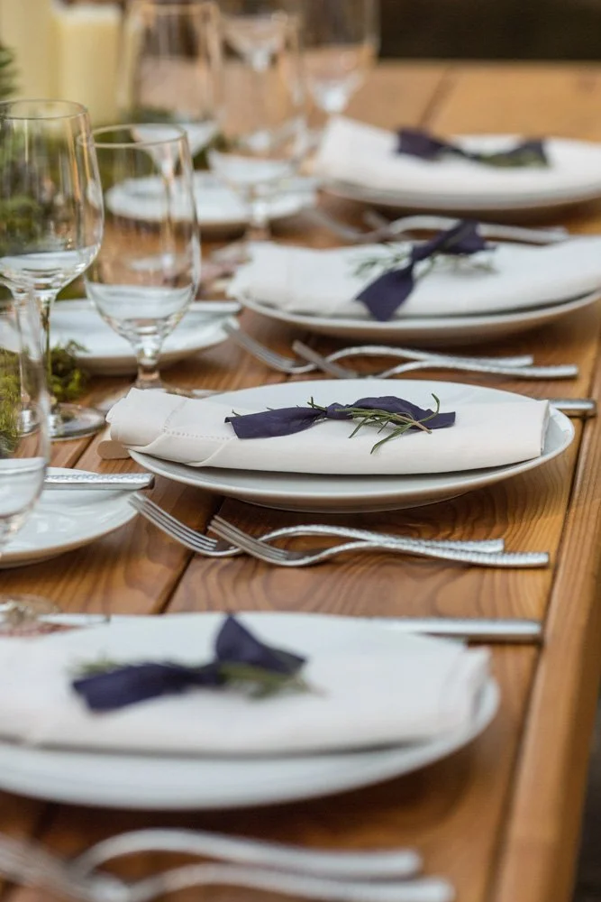 A close up of wedding place settings, simple and understated, on a wooden farm table designed by Simply Wed.