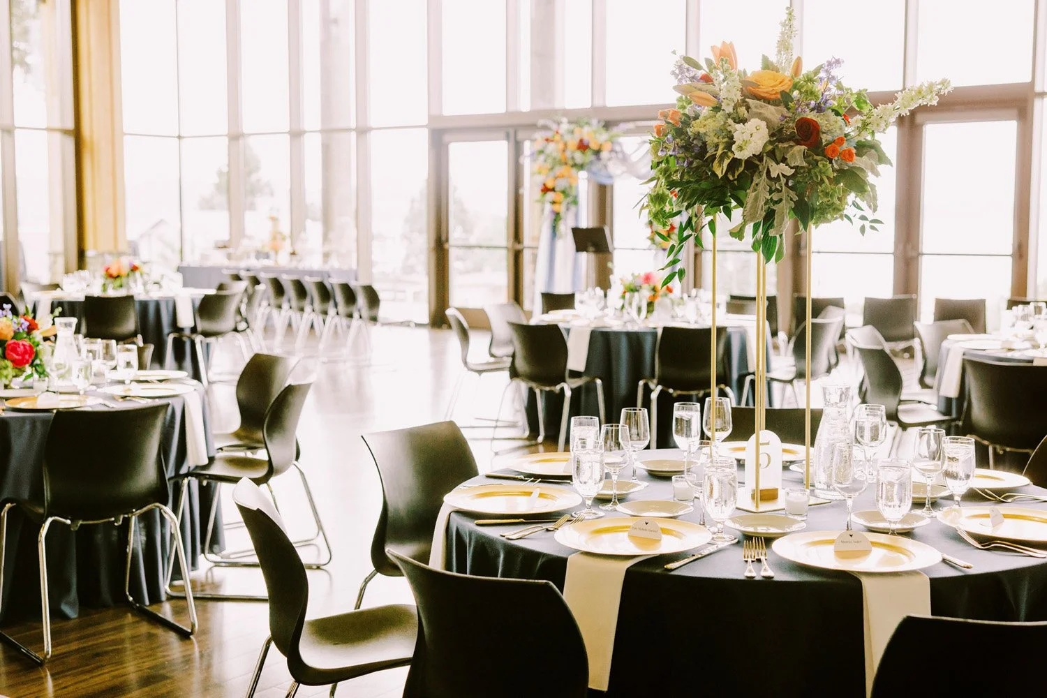 Round tables with navy table linens, gold plates and tall vibrant colored floral centerpieces Aviation boarding pass inspired seating place cards at the Rosehill Center-Photography by Jenn Tai & Co.-planned and designed by Simply Wed