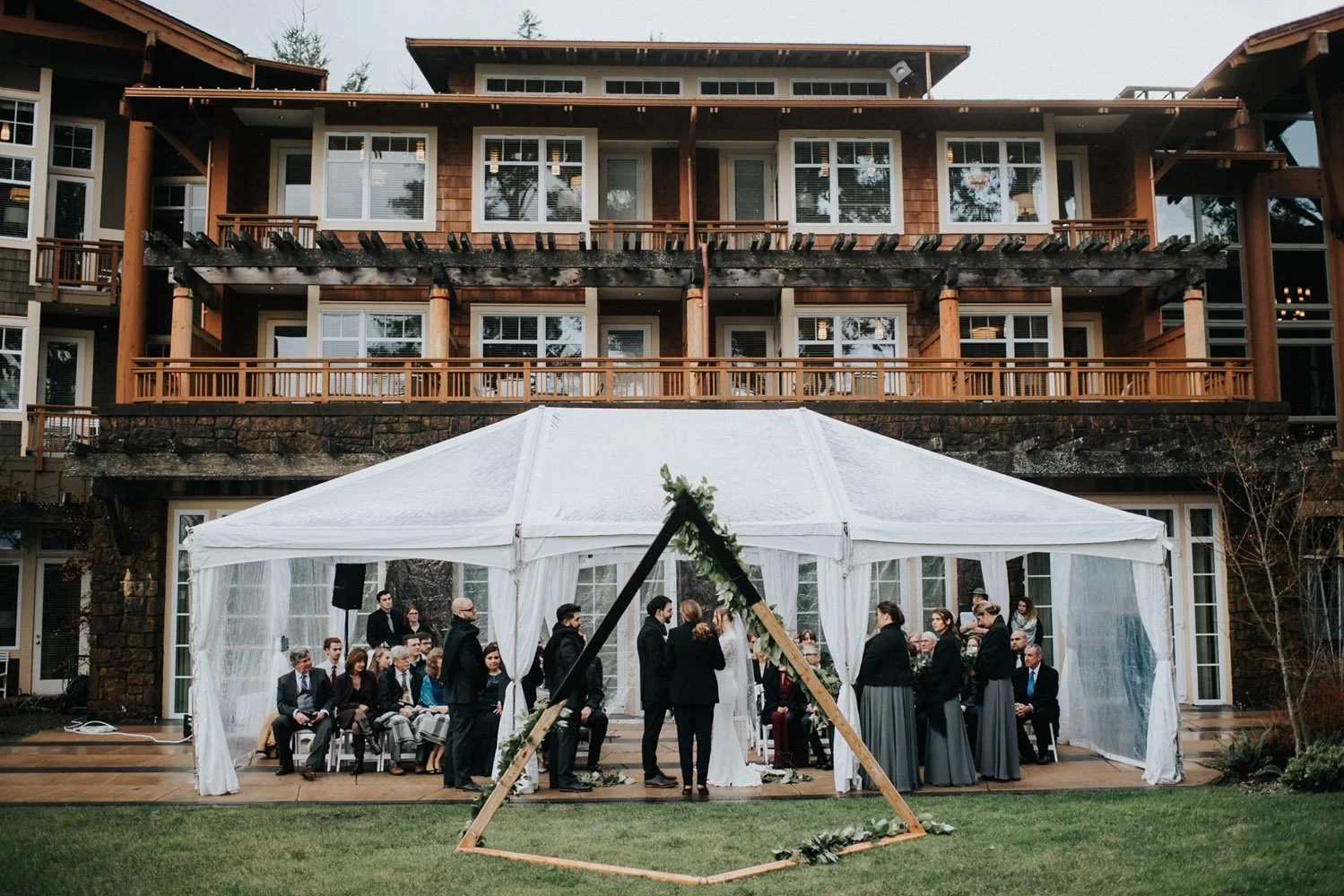 Bride and groom exchanging their vows and holding hands while guests watch under a white tent at their Gothic Rainforest wedding at the Alderbrook Resort-Photography by Nick plus Danee Photography.-planned and designed by Simply Wed